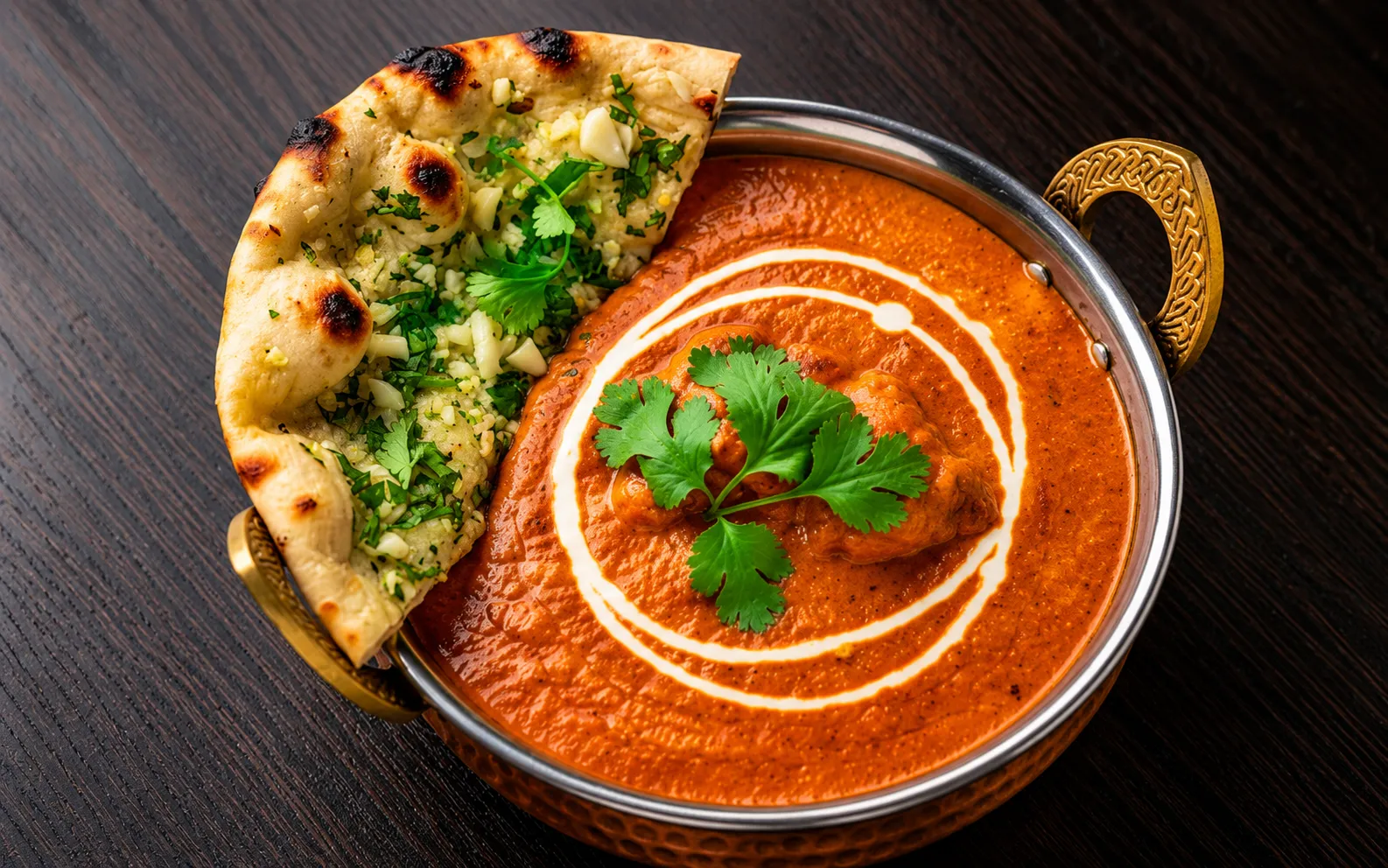 Indian butter chicken in creamy tomato-butter gravy, garnished with fresh coriander and cream, served with garlic naan.